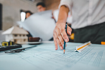 Eine Hand mit einem Bleistift, die auf einen Bauplan zeigt